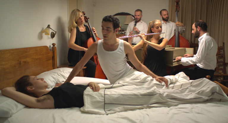 film still: klassisk orkester der spiller foran kvinde i hvid seng