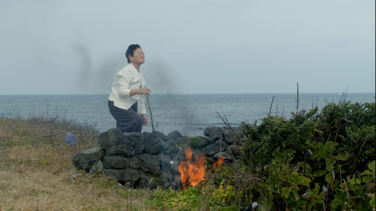 shamanistisk ritual udført af kvinde ved bål på stranden