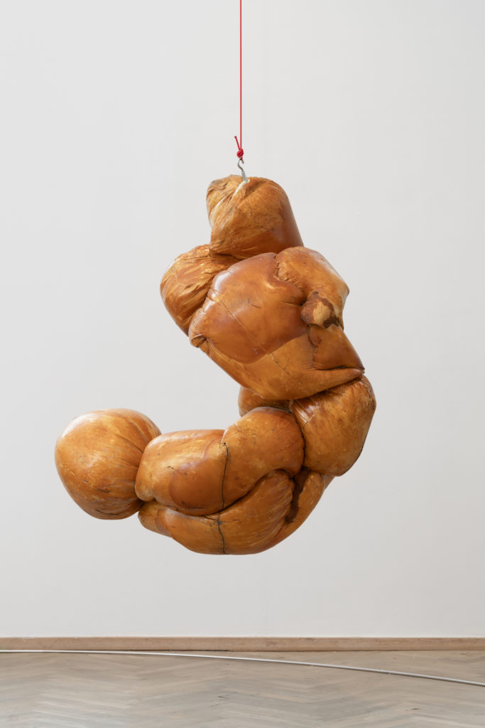 A sculpture in brown tones hangs in an exhibition space.