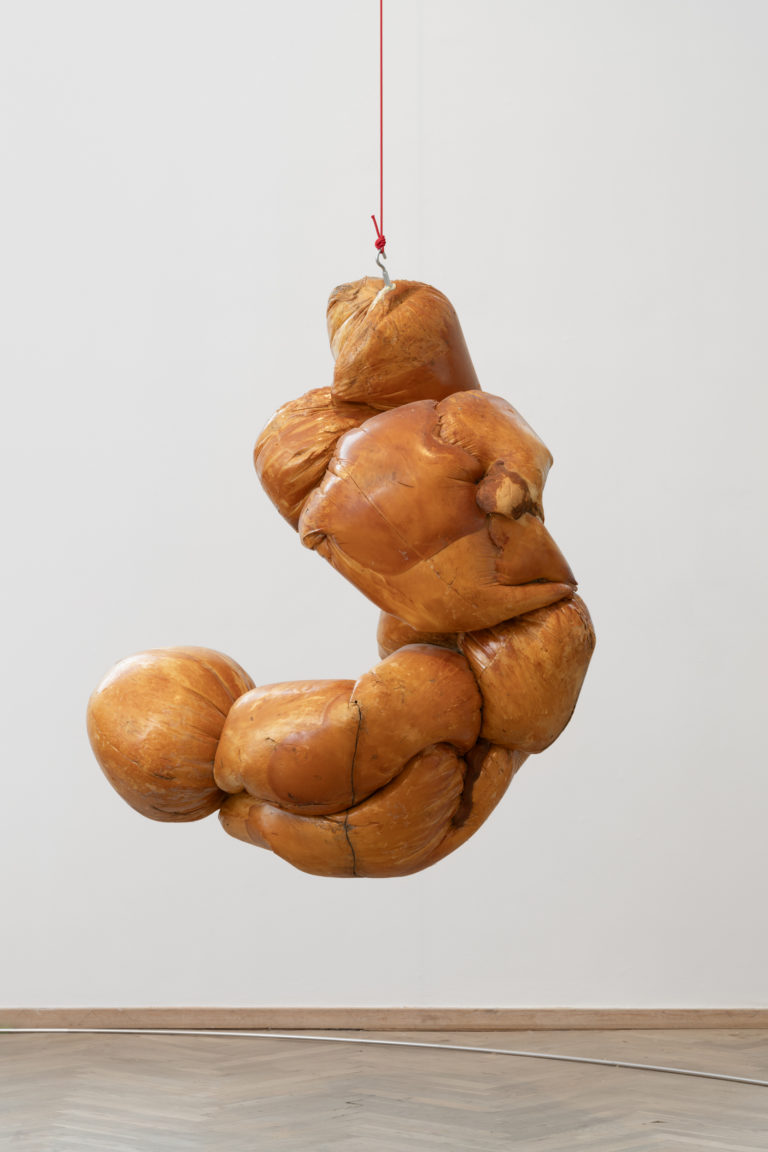 En skulptur i brune nuancer, hænger i et udstillingsrum.