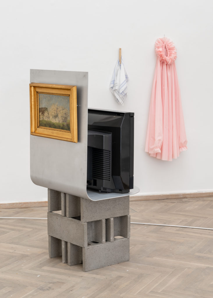 Exhibition view of a TV screen and a framed painting placed on a podium made of concrete blocks.