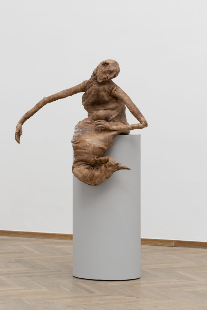 Havfruelignende skulptur, der sidder på et podium.