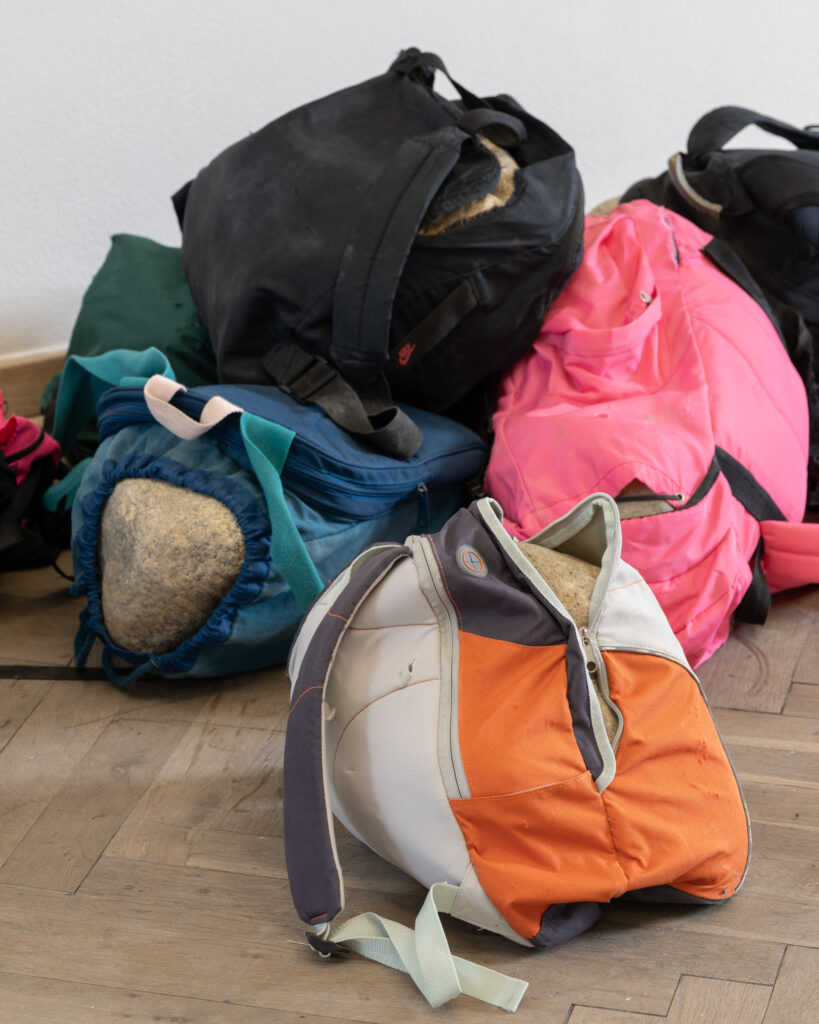 Backpacks in different colors, containing large stones.