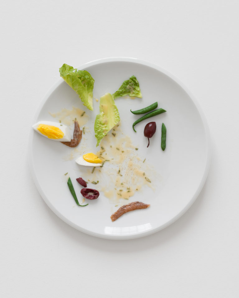 A white plate with a half-eaten egg, beans, olives, and anchovies.