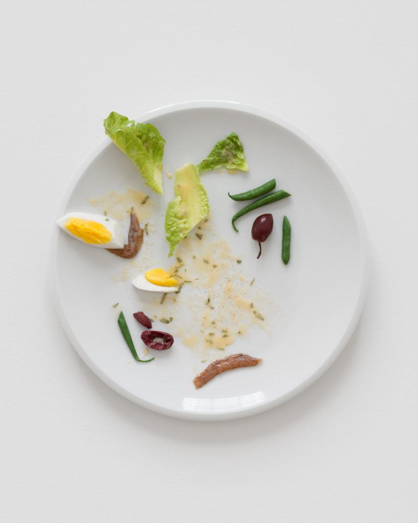 A white plate with a half-eaten egg, beans, olives, and anchovies.