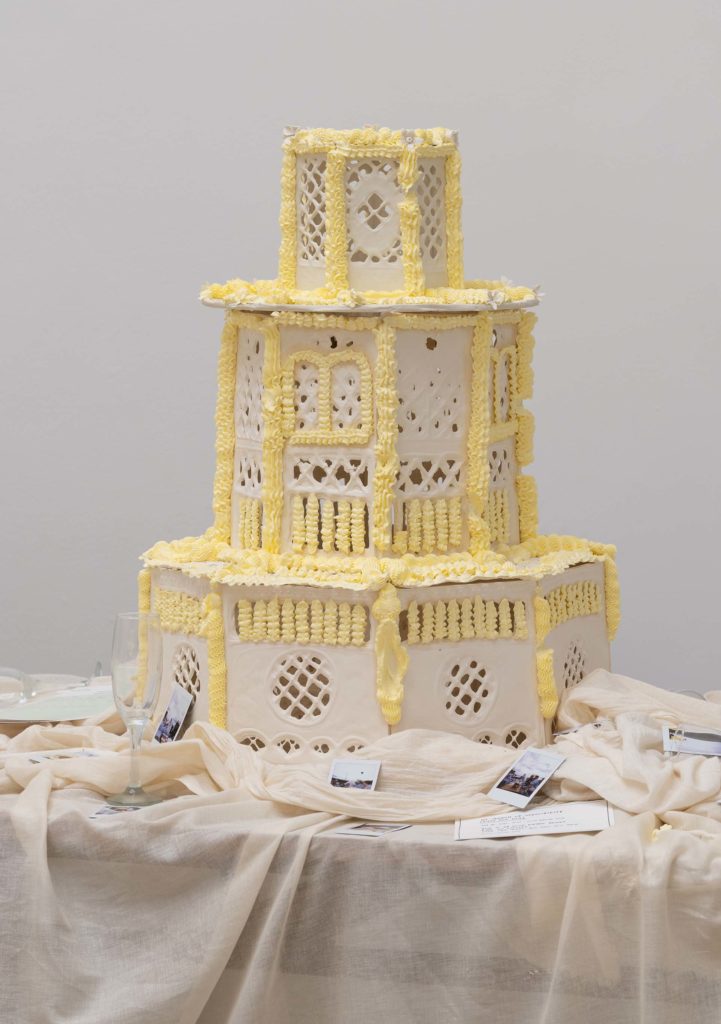 En bryllupskage, omgivet af en draperet dug og polaroid billeder.