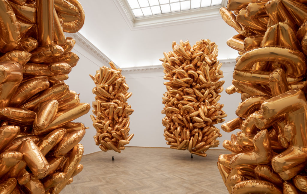 Four collections of gold balloons in an exhibition room.