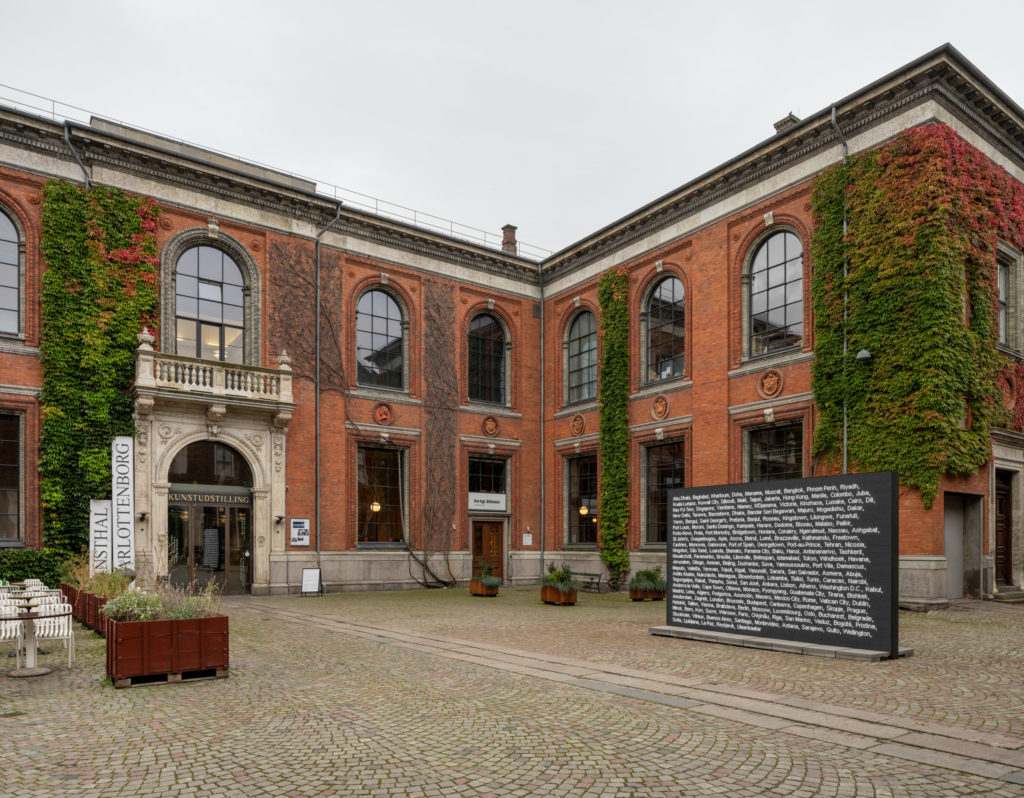 A courtyard with a screen displaying the names of cities.