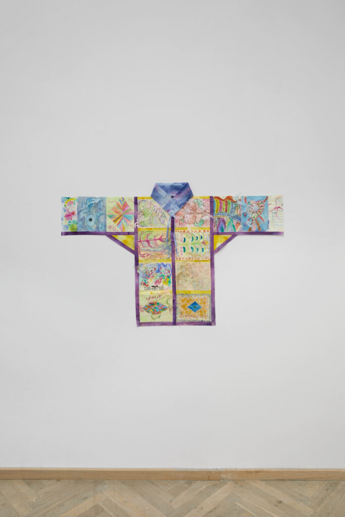 Farverig skjorte med illustrationer, hængt på væg.