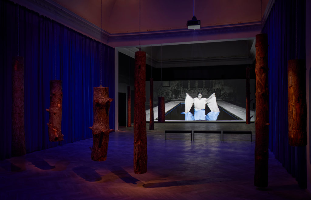 An exhibition space in blue tones, where a film is projected onto the wall.