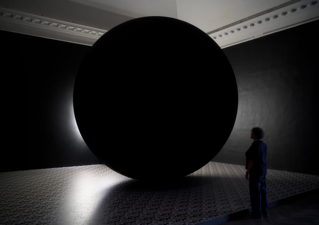 A black sphere stands in a dark exhibition space.